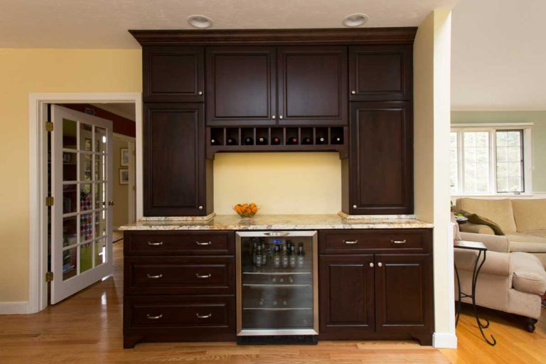 Dark wood home bar with a wine refrigerator and upper storage cabinets.