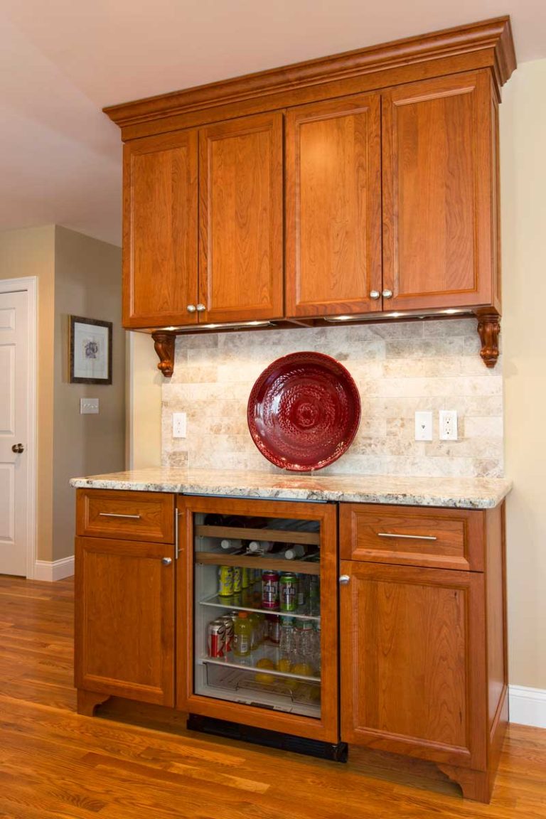 Wood home bar with a beverage refrigerator, glass-front cabinet and tile backsplash.