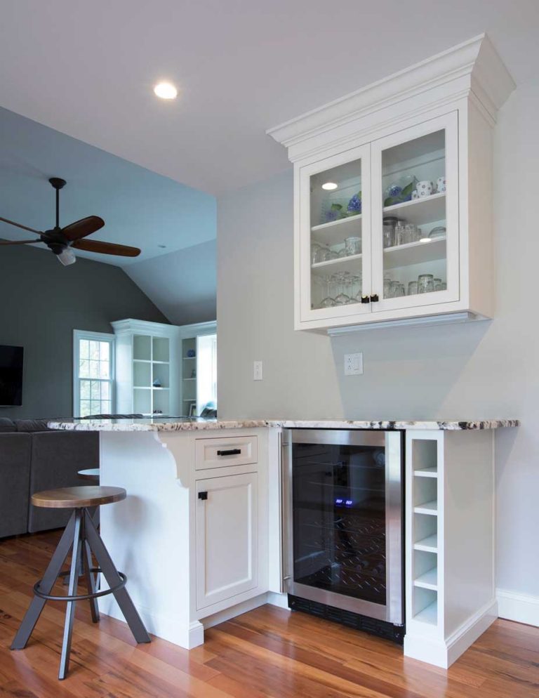 Built-in white home bar with a beverage refrigerator and glass-front cabinets.