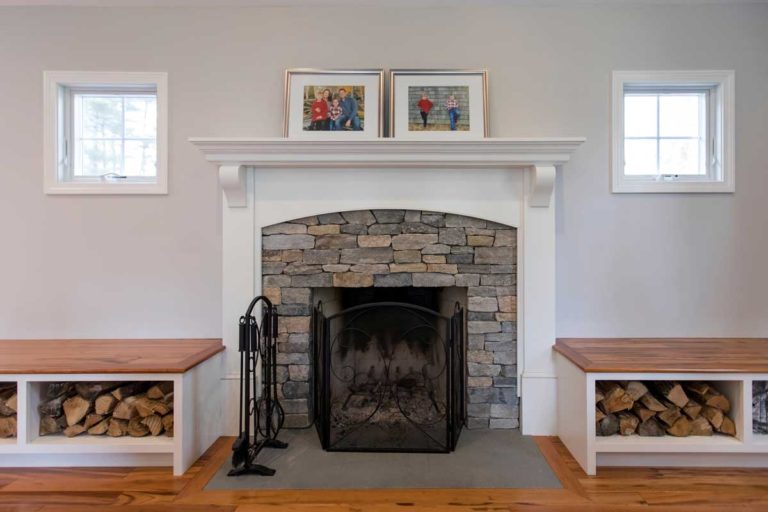 Stone fireplace with a white mantel and built-in firewood storage.