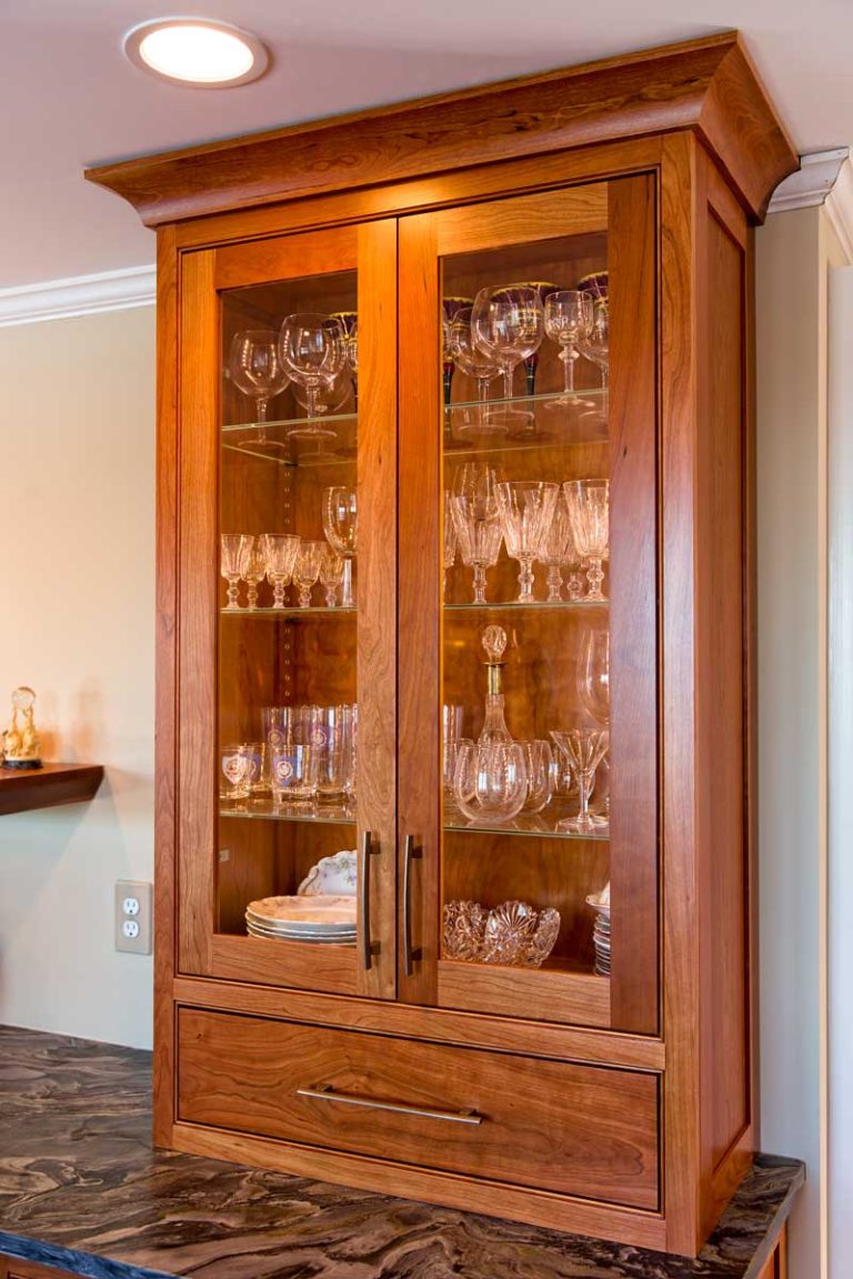 Wood display cabinet with glass-front doors for glassware.