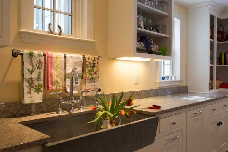 Laundry room sink with a dark countertop and white storage cabinets.