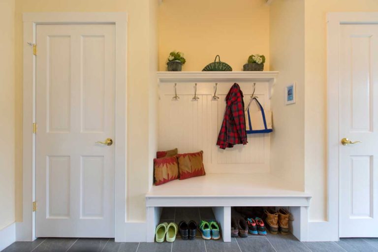 Mudroom bench with coat hooks, open shoe storage and white cabinetry.