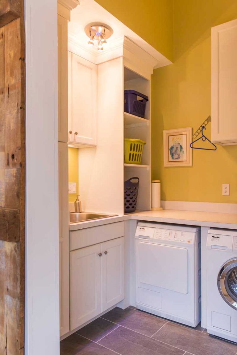 Laundry room with white cabinetry, washer and yellow walls.
