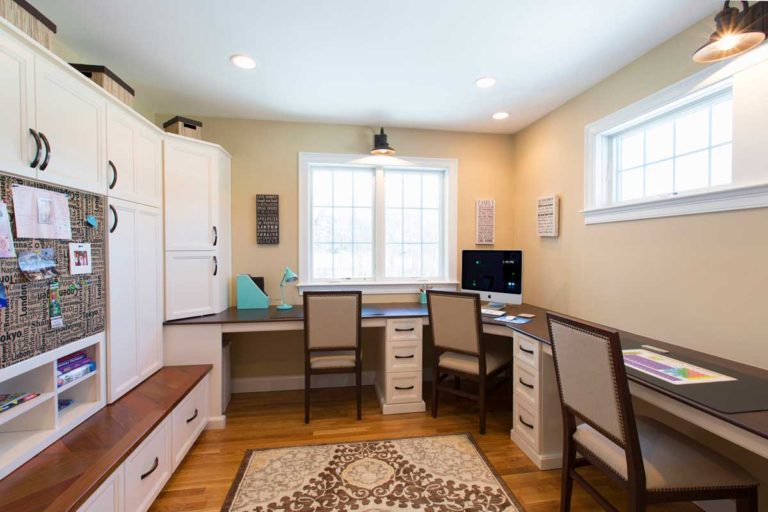 White home office cabinetry and desk beneath windows.