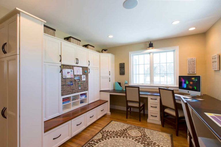 Home office with white cabinetry, a built-in desk and a cushioned bench.