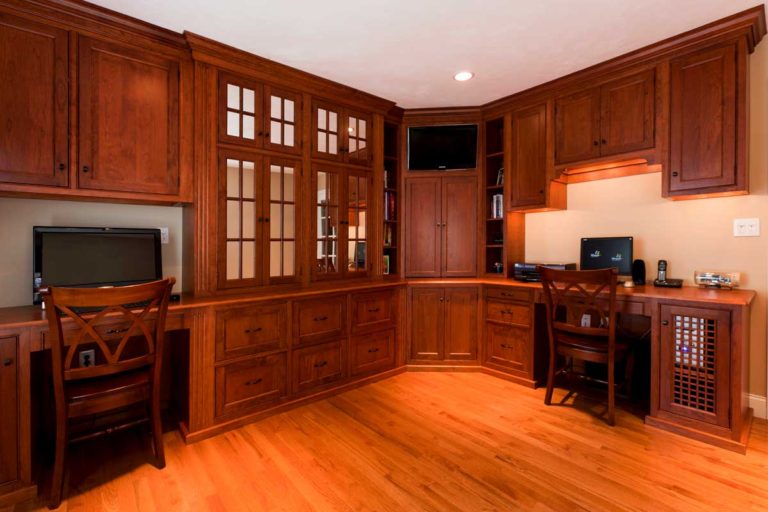 Home office with wood cabinetry, a built-in desk and glass-front cabinets.
