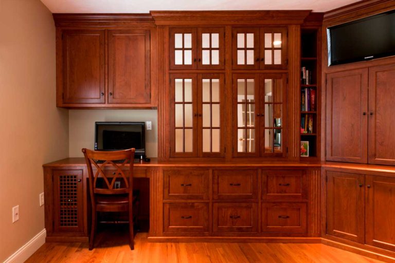 Home office wall with wood cabinetry, a built-in desk and television storage.